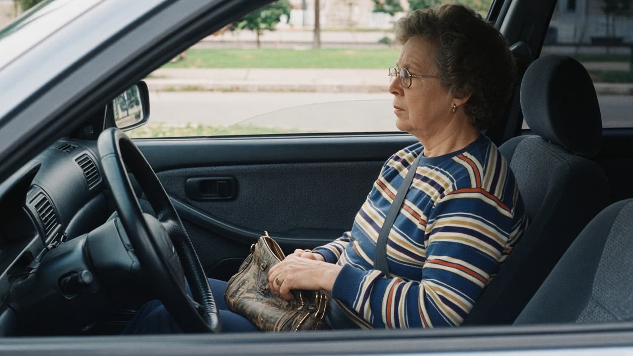 An older woman in glasses in the passenger seat of a parked car with a purse on her lap